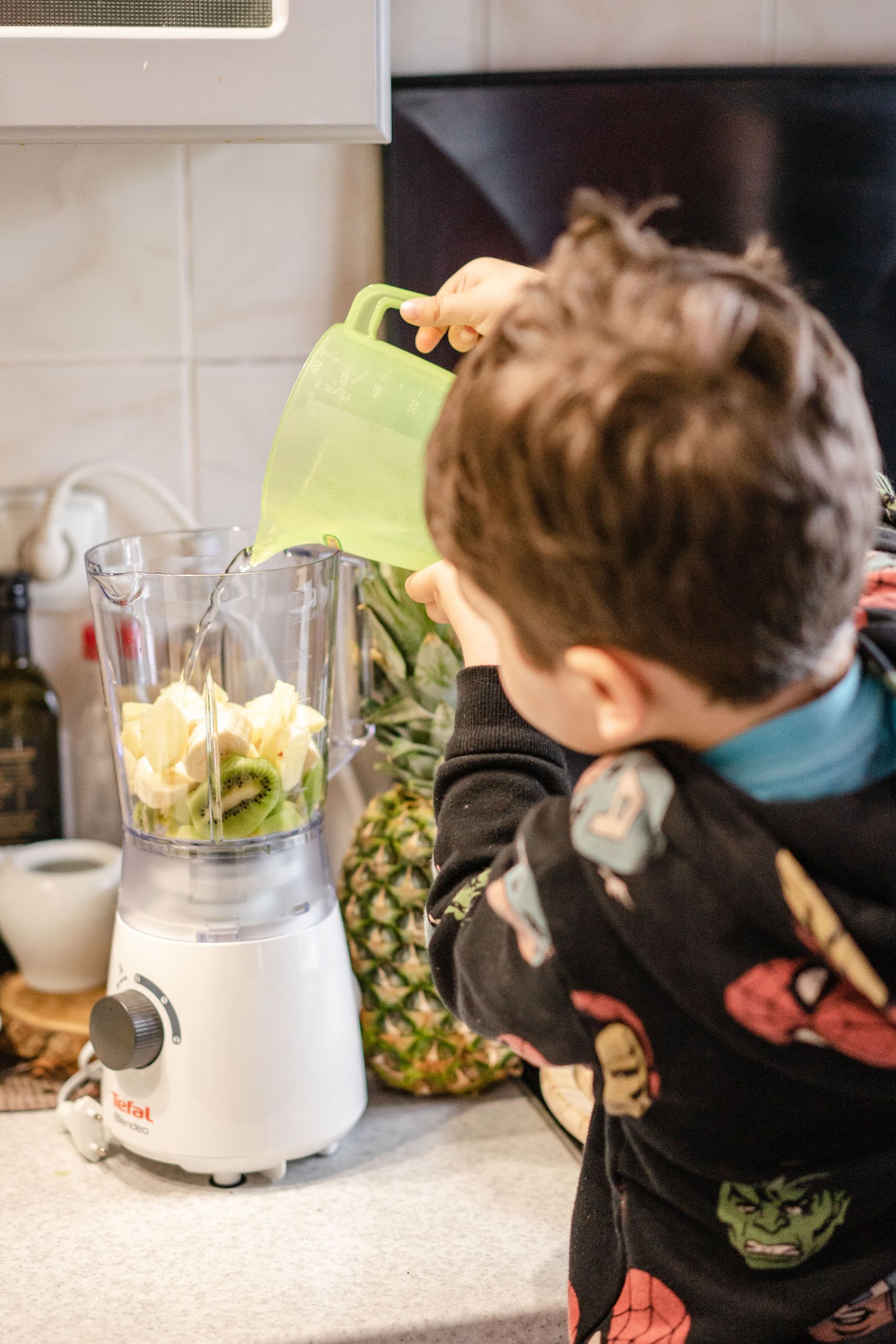 A child pours ingredients into a blender to make a fresh fruit smoothie.